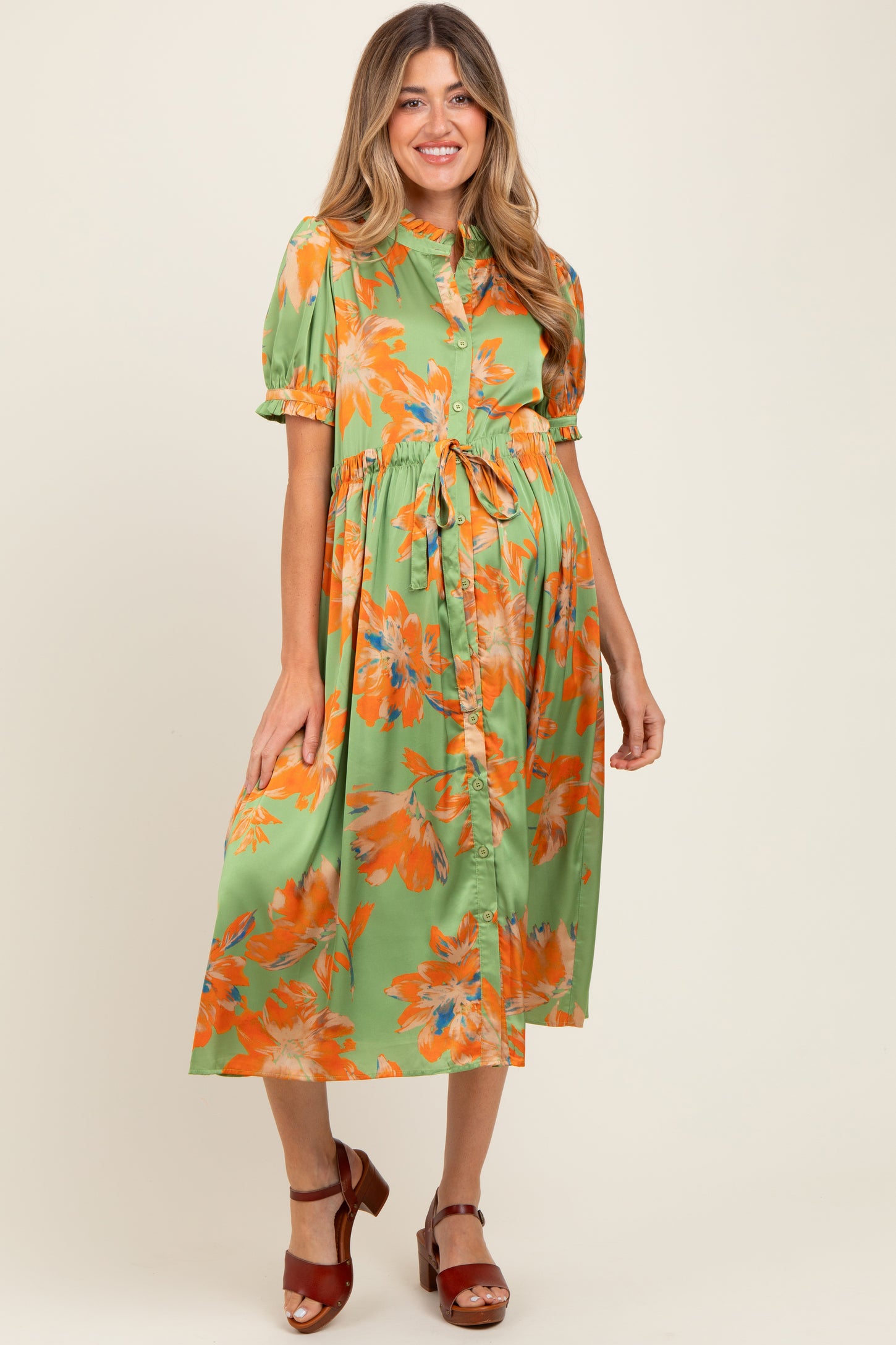 woman wearing a green floral maternity dress with short sleeves and a tie waist, showcasing her baby bump