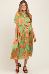 woman wearing a green floral maternity dress with short sleeves and a tie waist, showcasing her baby bump