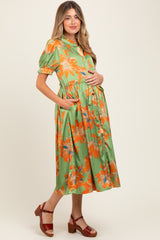 woman wearing a green floral maternity dress with short sleeves and a gathered waist, holding her baby bump