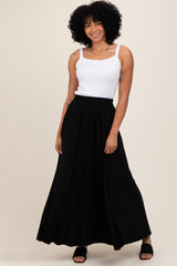 woman wearing a white tank top and a black maxi skirt, standing with a smile against a neutral background