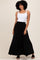 woman wearing a white tank top and a black maxi skirt, standing with a smile against a neutral background