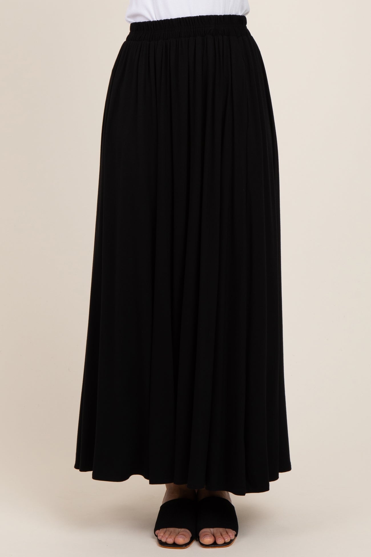 woman wearing a black pleated maxi skirt with an elastic waistband and flat sandals
