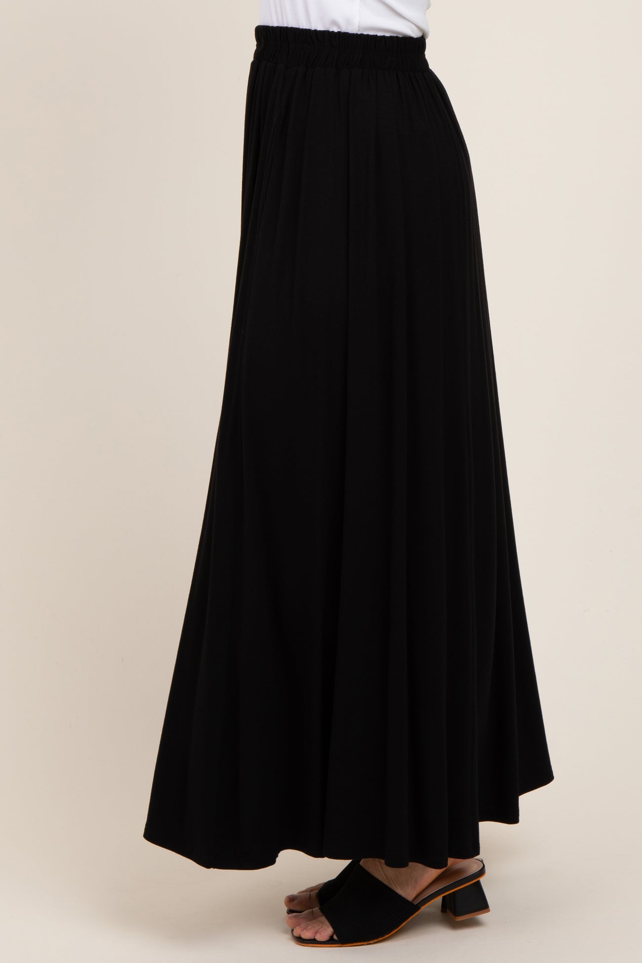 woman wearing a black maxi skirt with an elastic waistband and flowy silhouette, viewed from the side