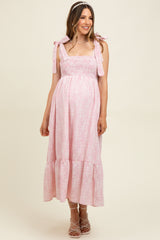 woman wearing a light pink floral maternity dress with bow straps and a flared skirt, showing her baby bump