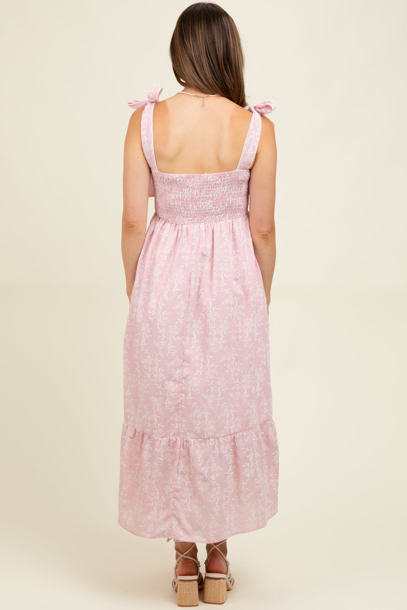 woman wearing a pink floral maternity maxi dress with smocked bodice and tie straps, showing her back