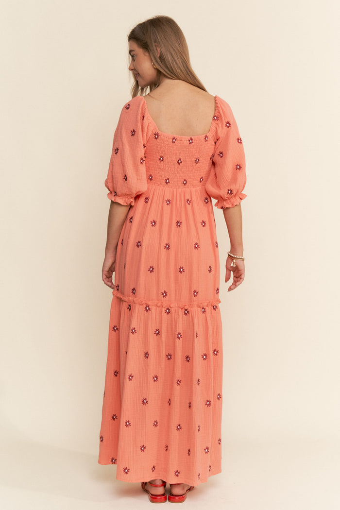 woman wearing a coral maxi dress with floral embroidery and puff sleeves, shown from the back
