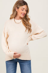 woman wearing a cream oversized maternity sweater with a baby bump and styled with denim jeans
