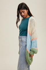 woman wearing a multicolored oversized knit cardigan over a teal top and high-waisted light blue jeans