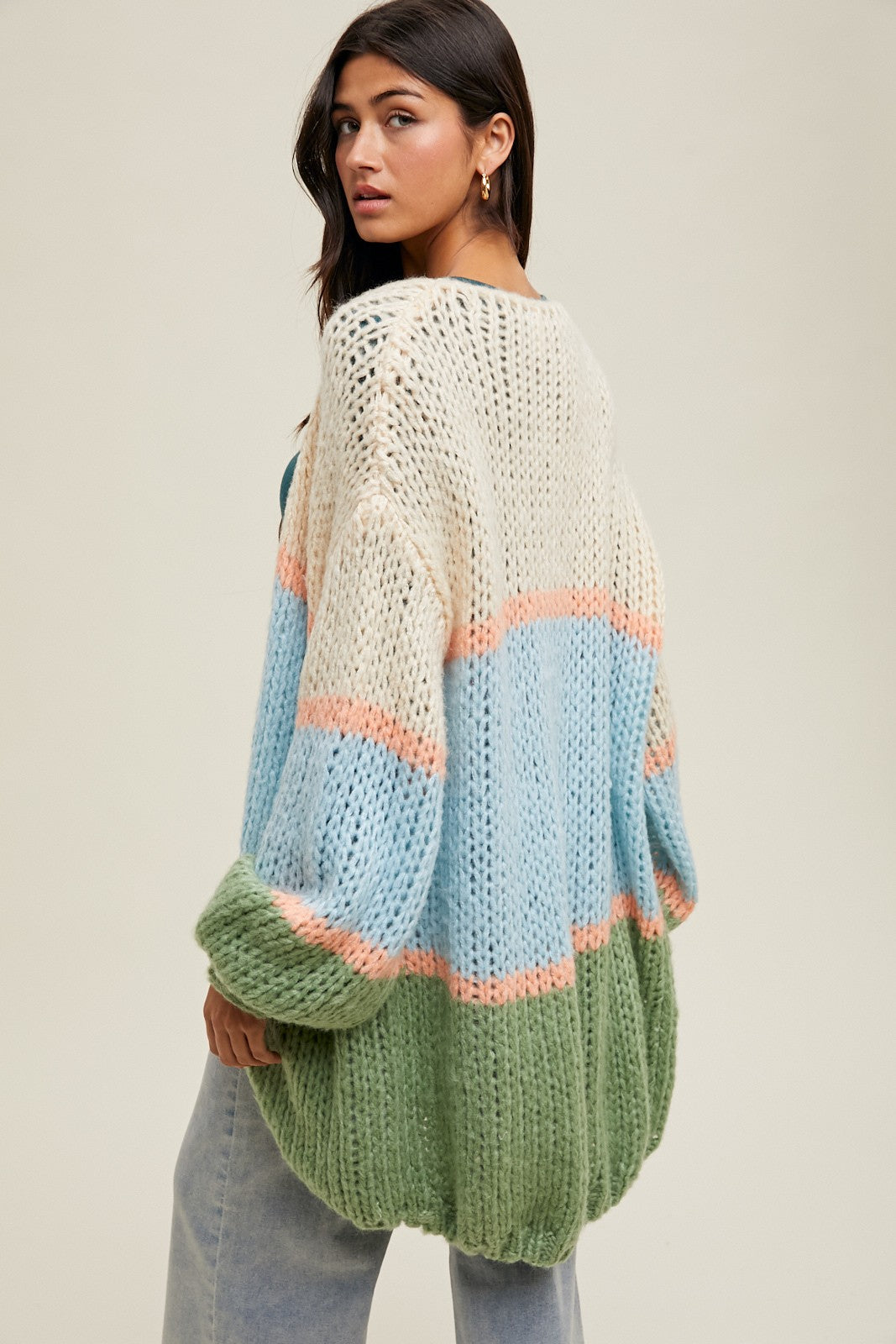 woman wearing an oversized multi-colored knit cardigan with blue, peach, and green stripes, styled with loose jeans