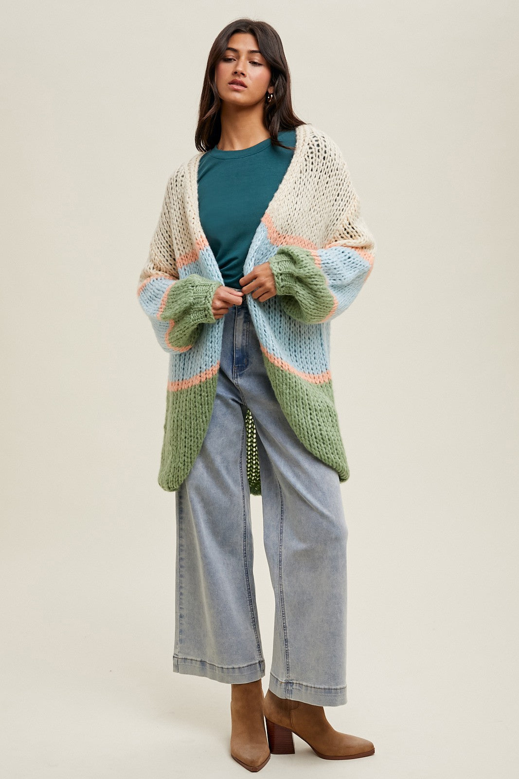 woman wearing a multi-color oversized chunky knit cardigan with bell sleeves, paired with a green top and wide-leg jeans