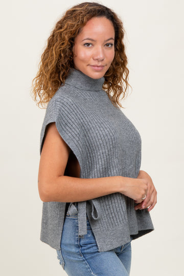 woman wearing a gray sleeveless turtleneck sweater with side ties and a ribbed texture, standing sideways