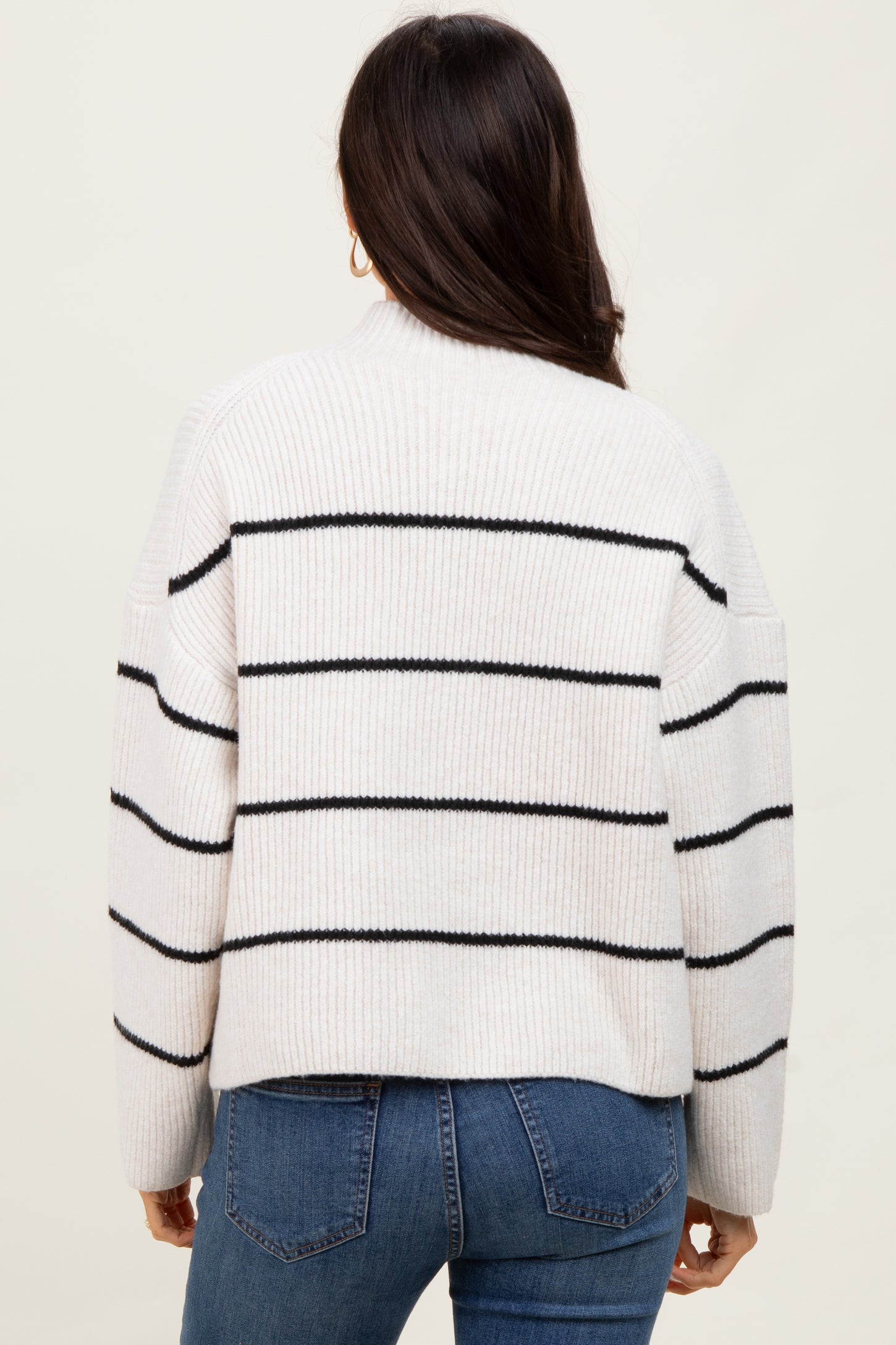 woman wearing a cream striped oversized sweater with black stripes, paired with blue jeans, view from the back