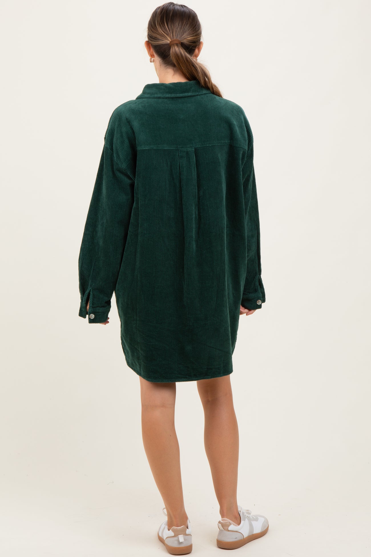 woman wearing a dark green corduroy maternity dress with long sleeves and a relaxed fit from the back