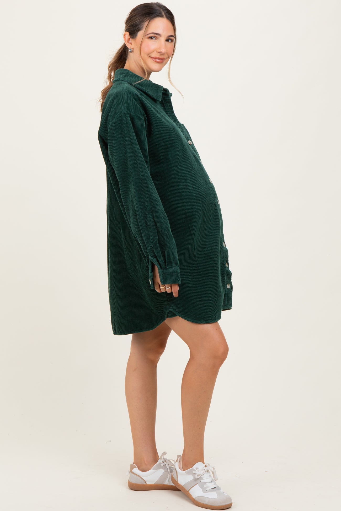 woman wearing a green corduroy maternity shirt dress with a visible baby bump and white sneakers