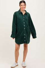 woman wearing a dark green corduroy maternity shirt dress with a collar and buttons, standing against a neutral background