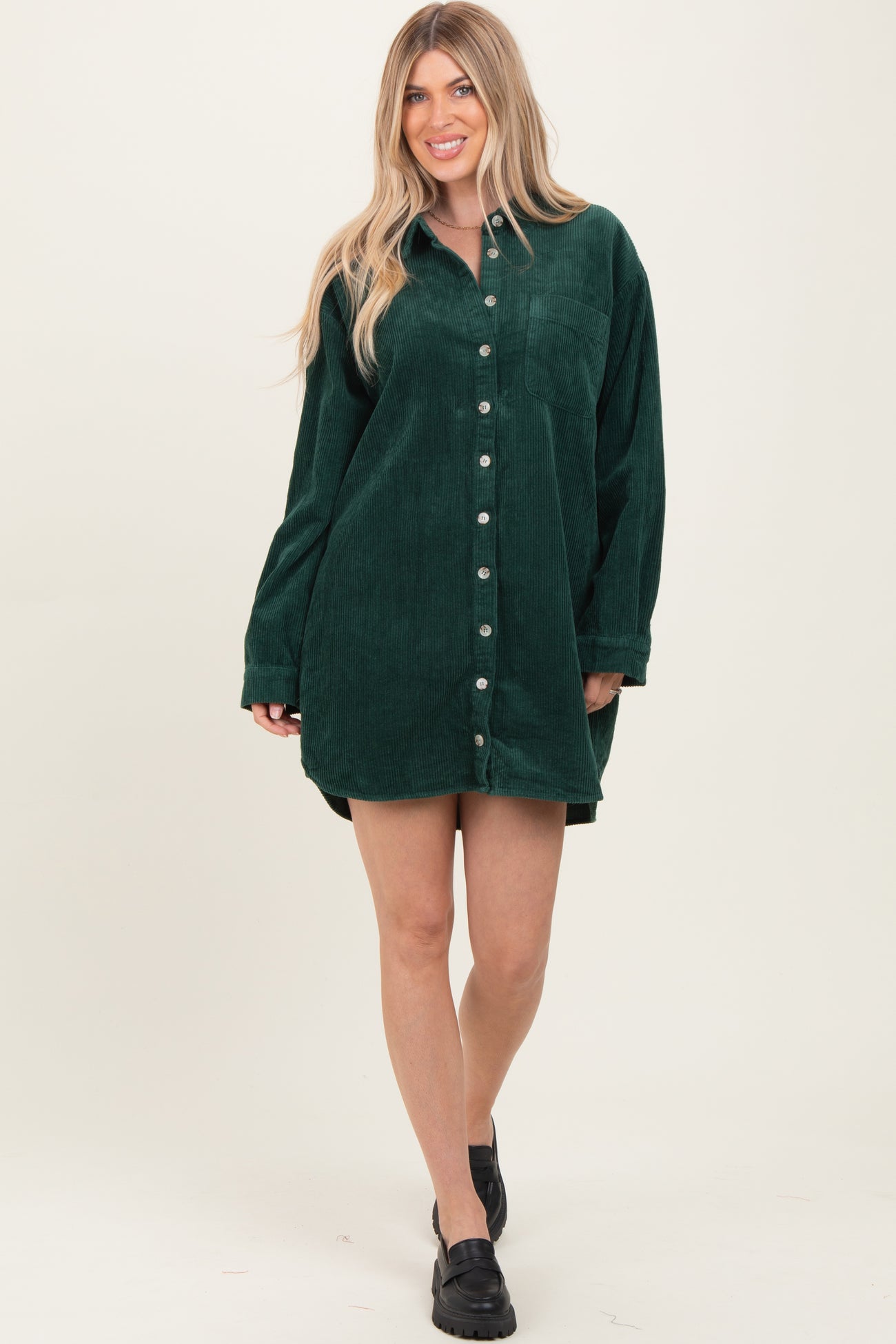 woman wearing a green corduroy shirt dress with buttons and long sleeves, standing and smiling