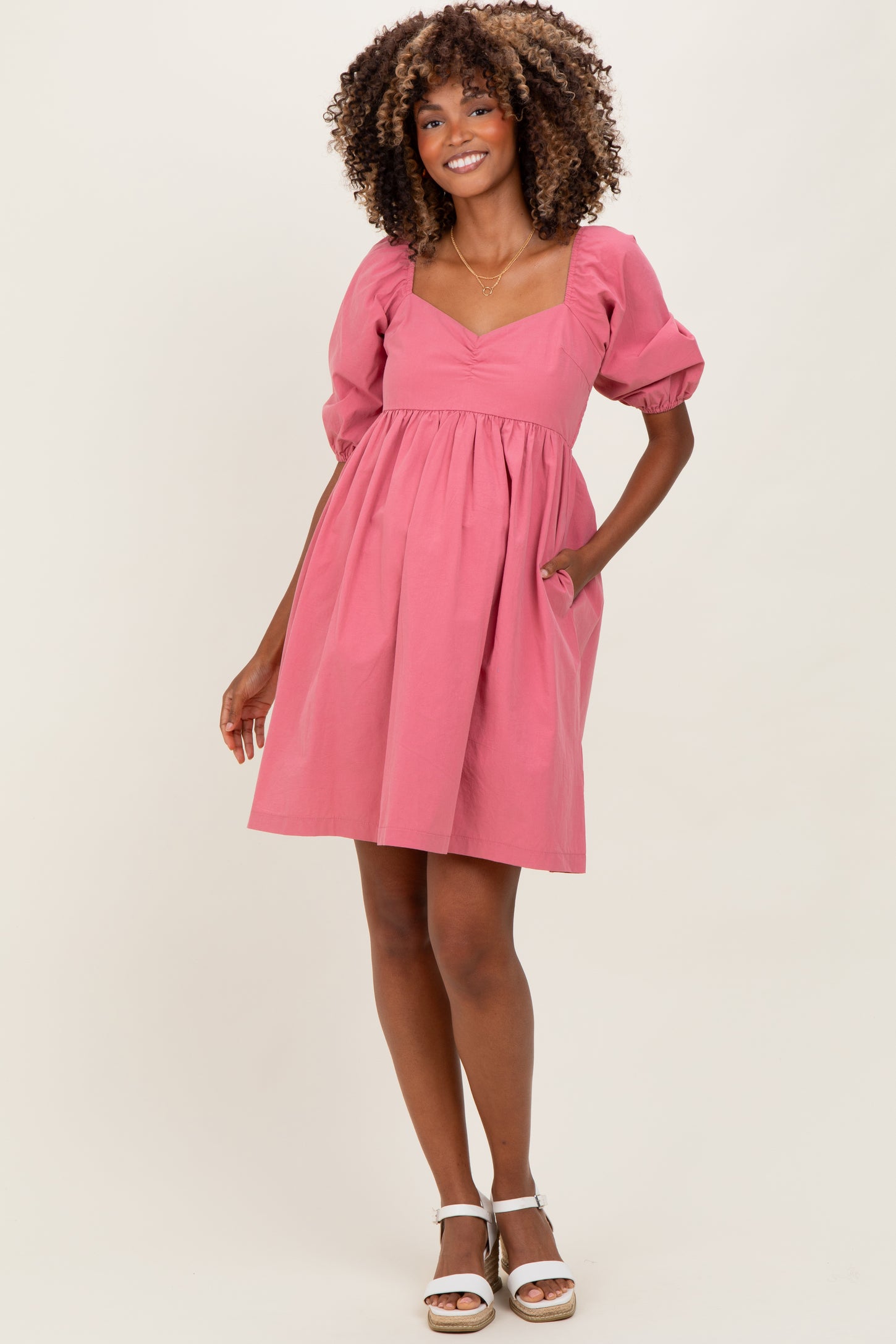 woman wearing a pink puff sleeve maternity dress with a sweetheart neckline and pockets