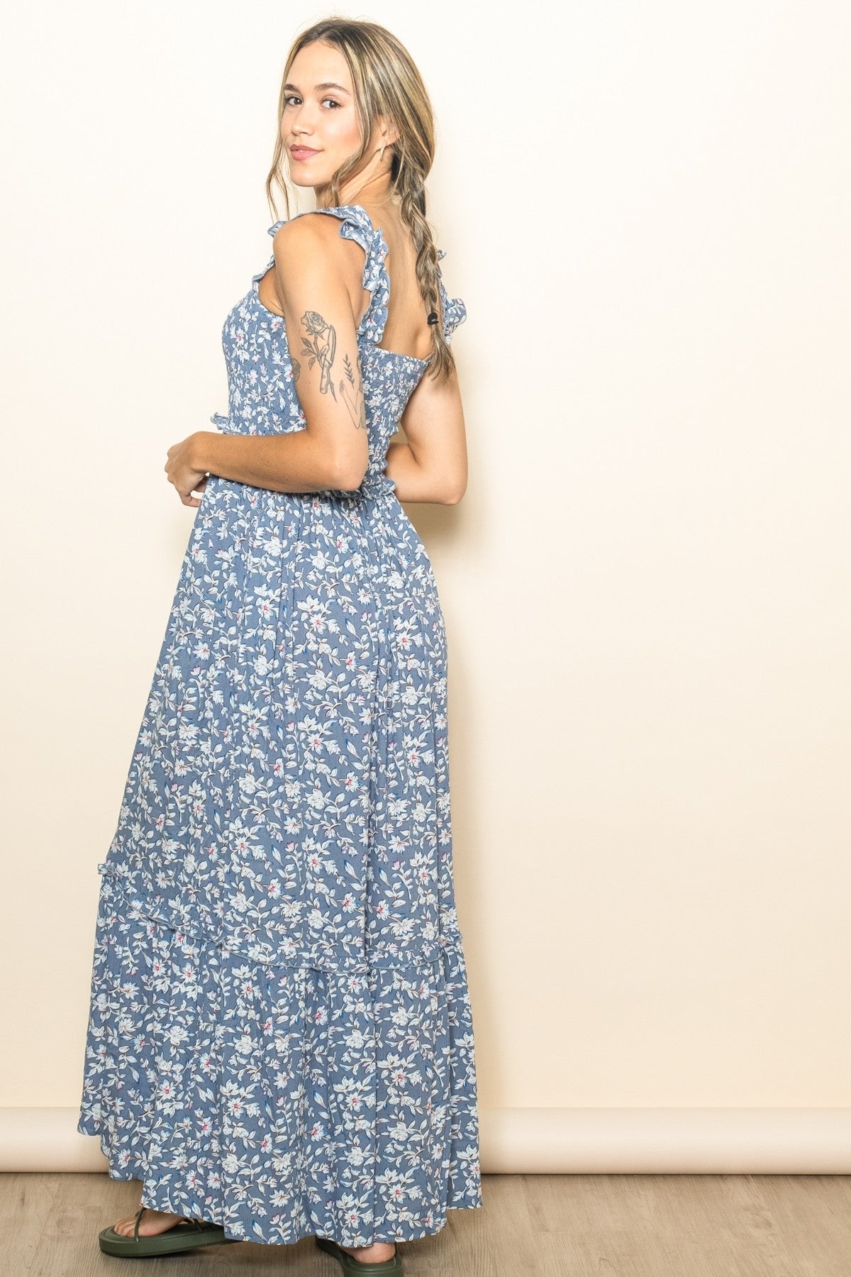 woman wearing a blue floral maxi dress with ruffled straps and a tiered skirt, standing sideways against a light background