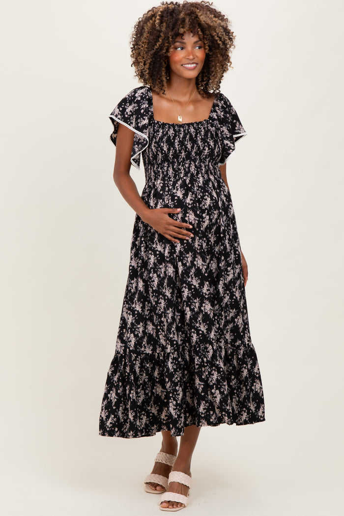 woman wearing a black floral print maternity maxi dress and holding her baby bump