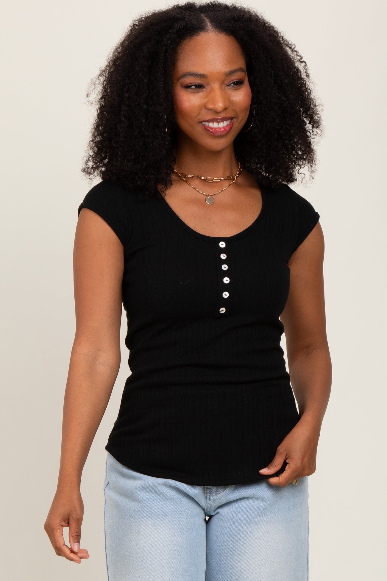 woman wearing a black ribbed scoop neck top with cap sleeves and button details, paired with light blue jeans