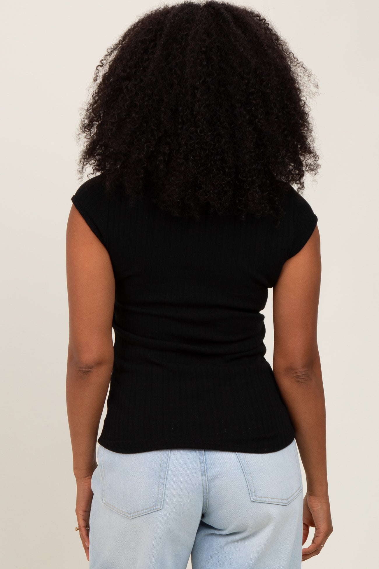 woman wearing a black ribbed cap sleeve top and light blue high-waisted jeans, seen from the back