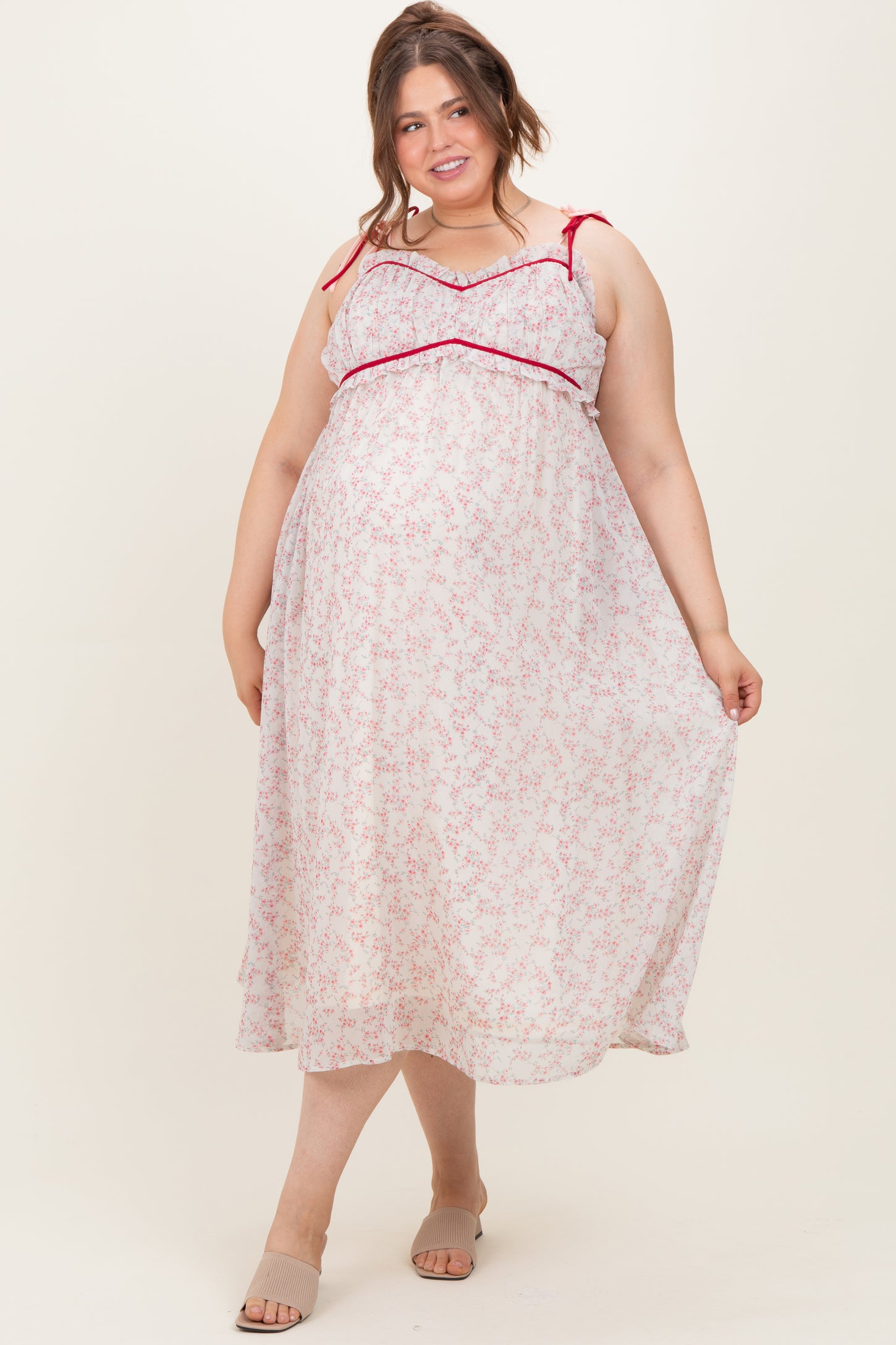 woman wearing a floral print maternity plus maxi dress with red accents and a visible baby bump