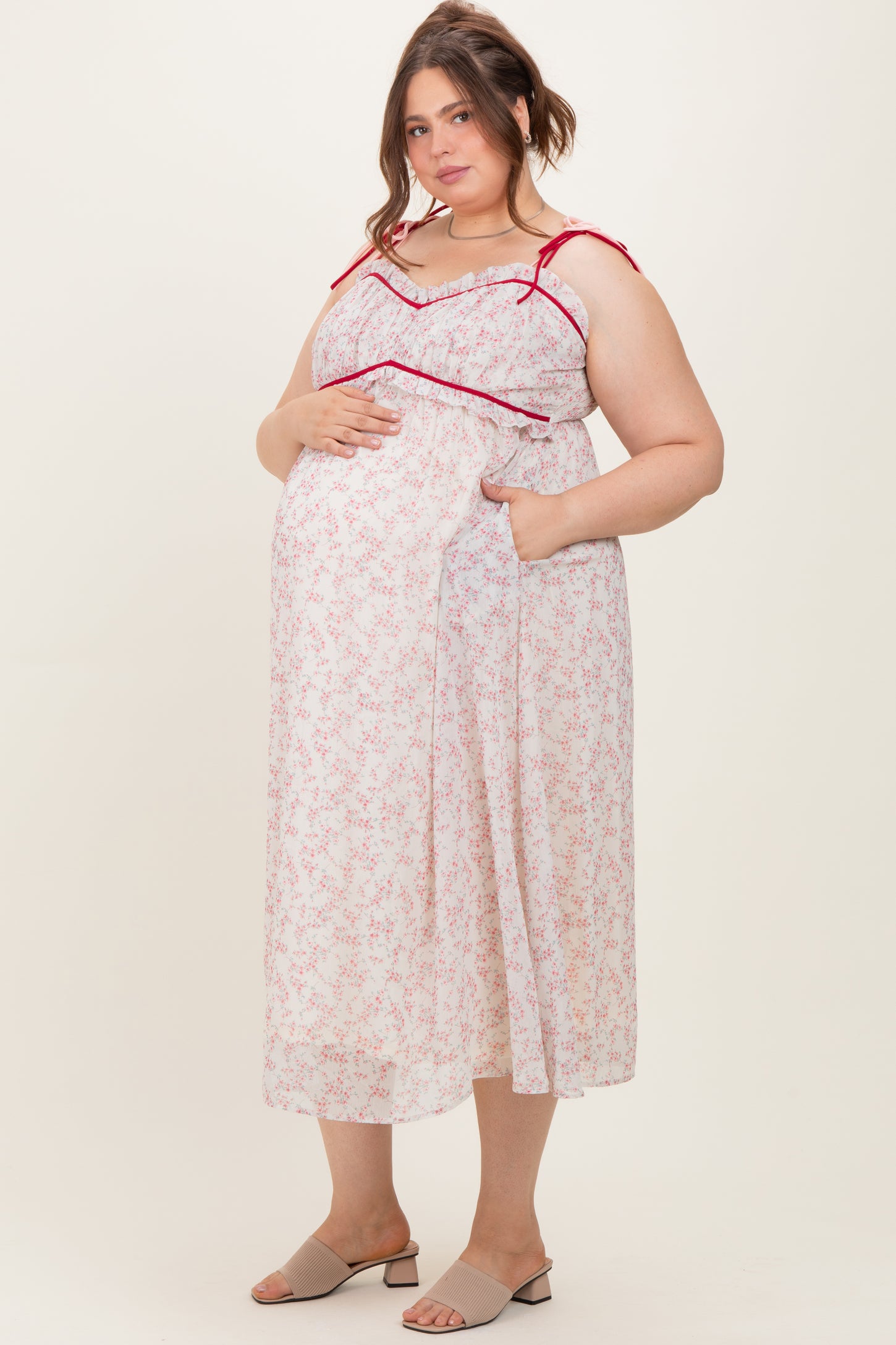 woman wearing a floral sleeveless maternity dress with red straps and pockets, showing her baby bump