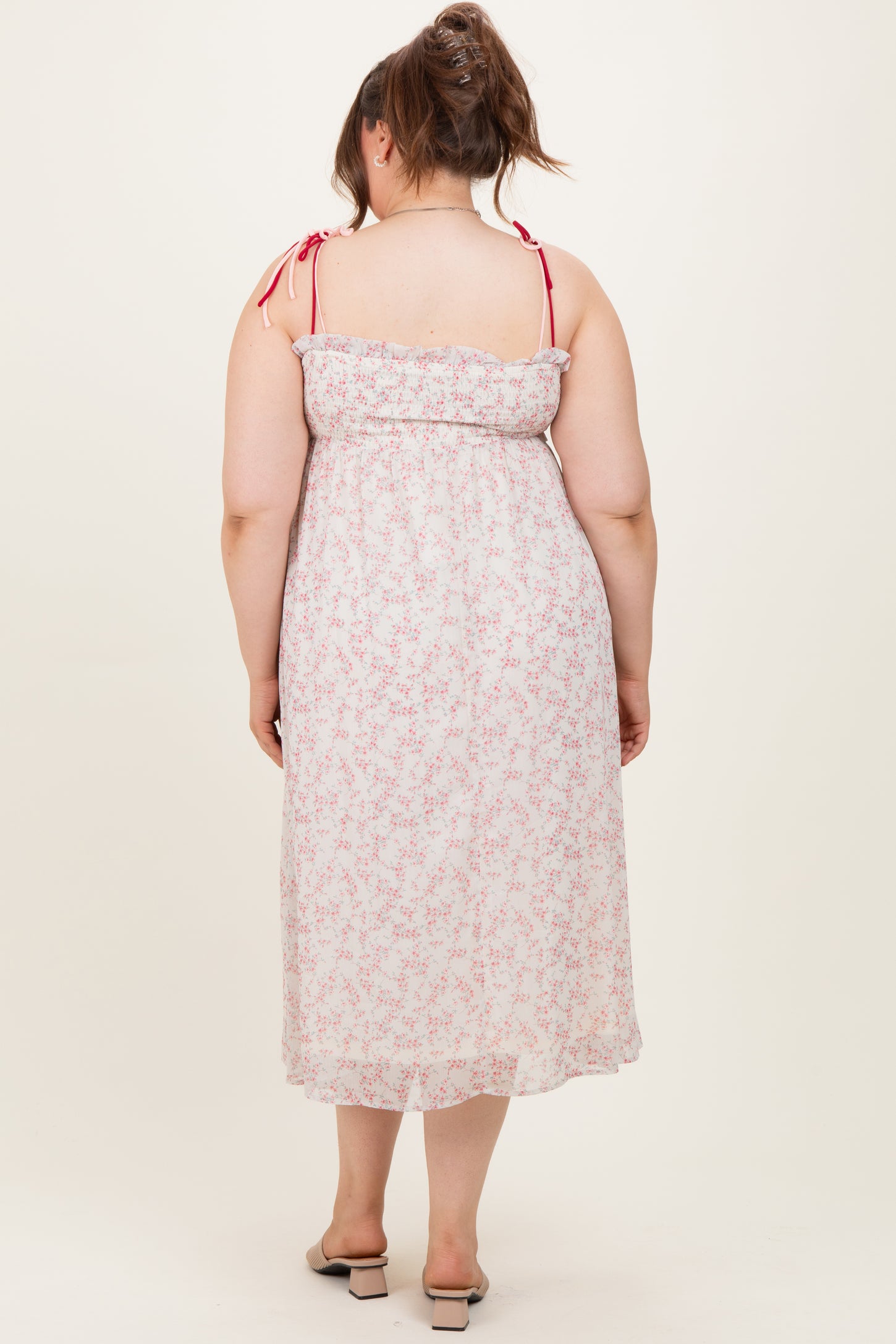 woman wearing a floral maternity plus midi dress with adjustable straps and ruffle detailing, viewed from the back