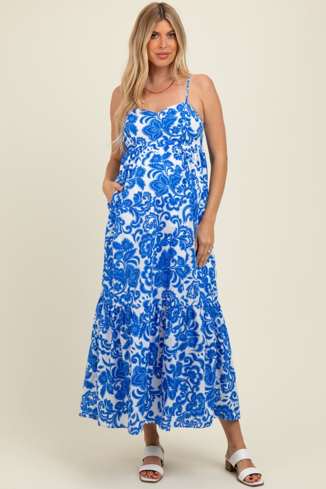 woman wearing a blue and white floral maternity maxi dress with pockets and adjustable straps, showing her baby bump