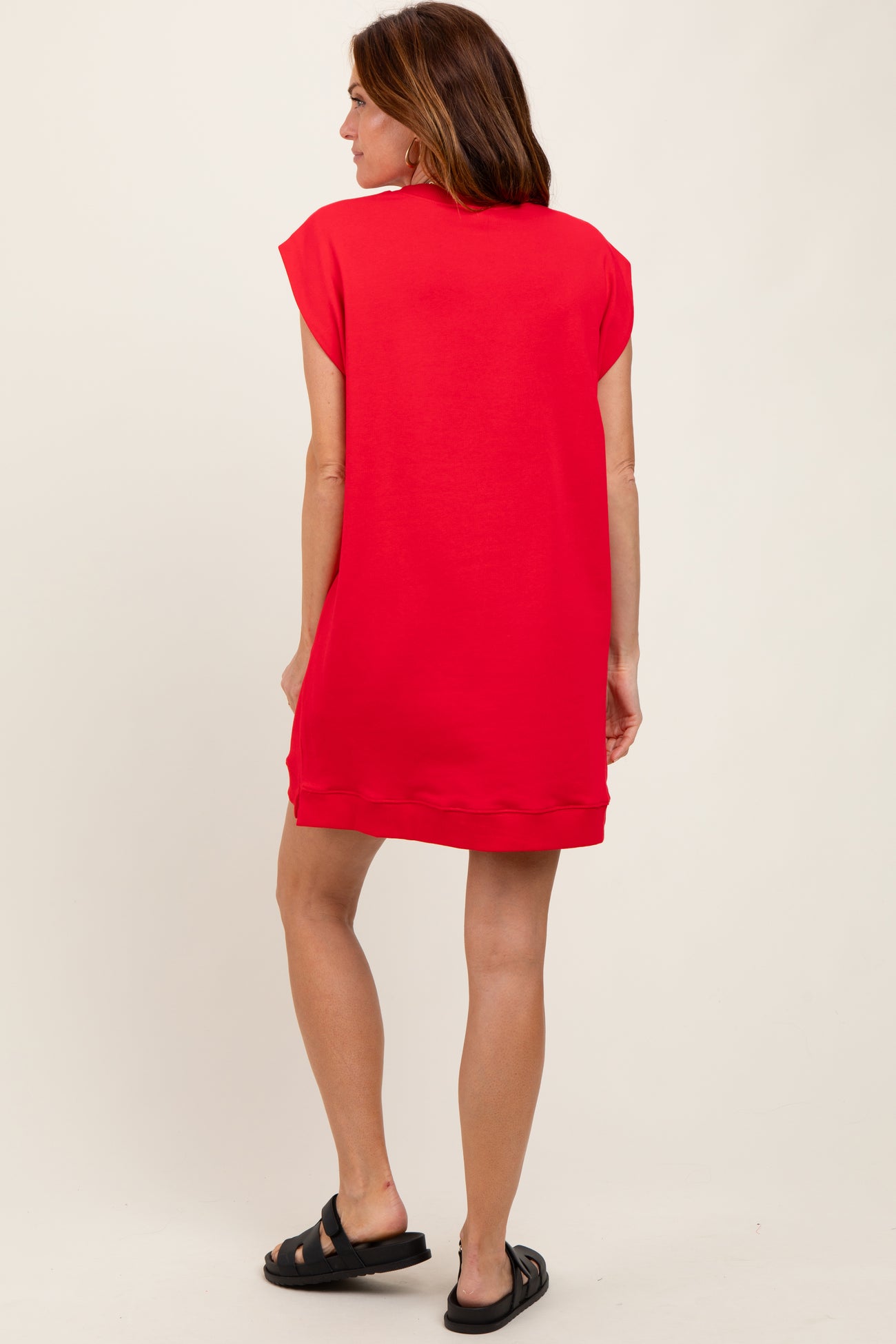 woman wearing a bright red short sleeve sweatshirt dress, seen from the back, styled with black slide sandals