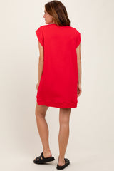 woman wearing a bright red short sleeve sweatshirt dress, seen from the back, styled with black slide sandals