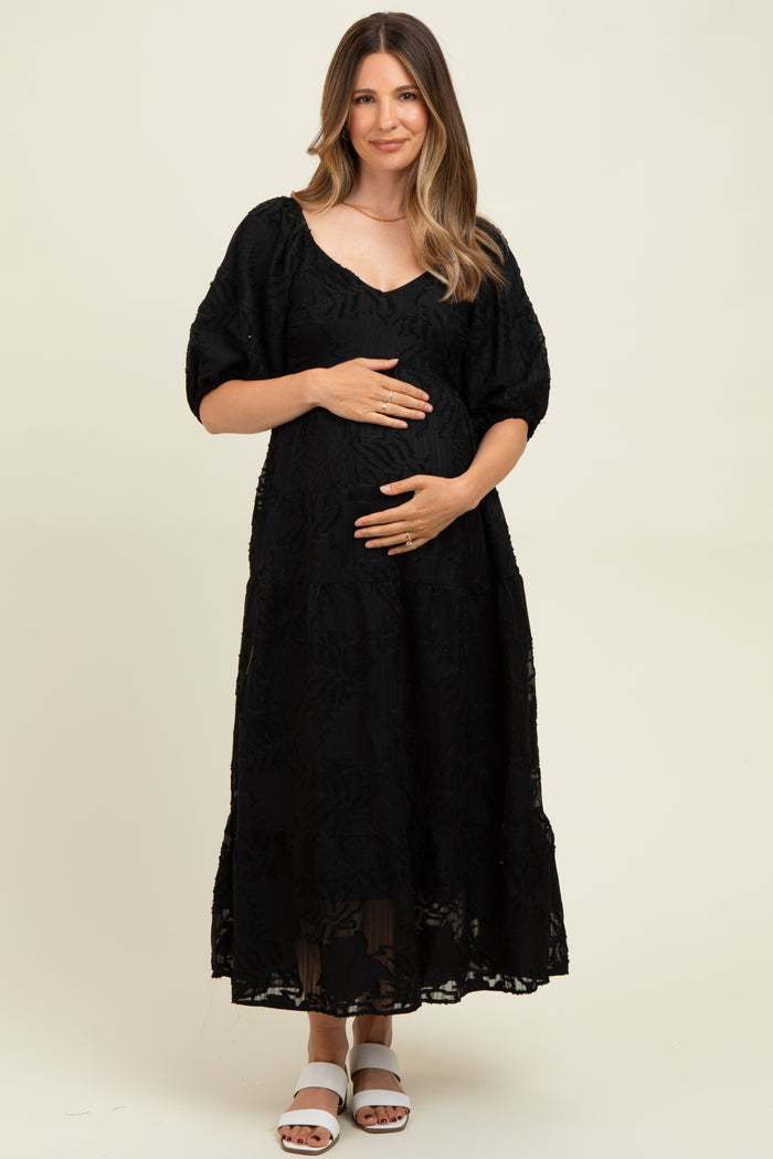 woman wearing a black lace maternity dress with puff sleeves and holding her baby bump