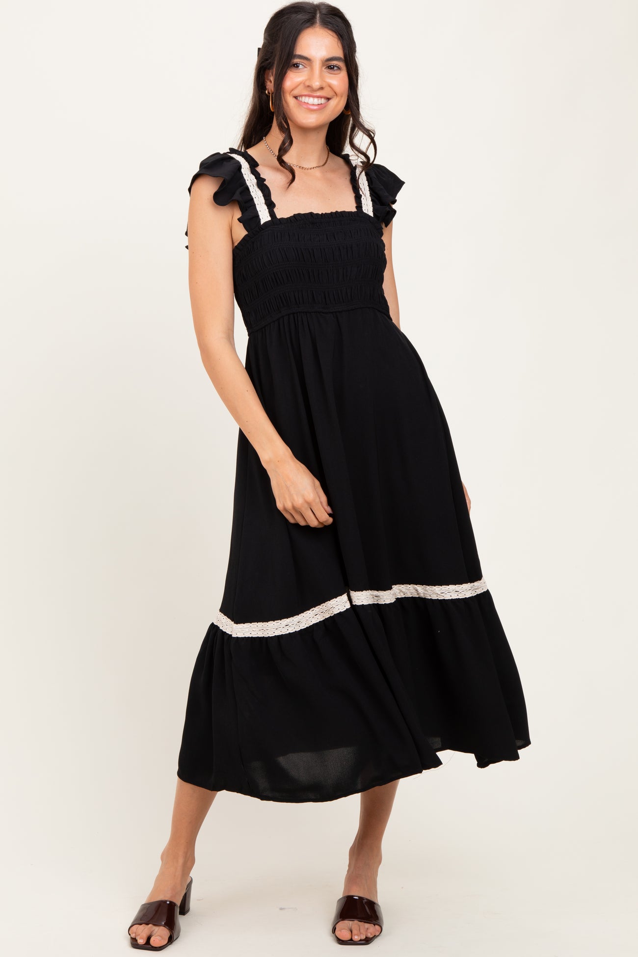 woman wearing a black smocked midi dress with ruffled shoulder straps and lace trim