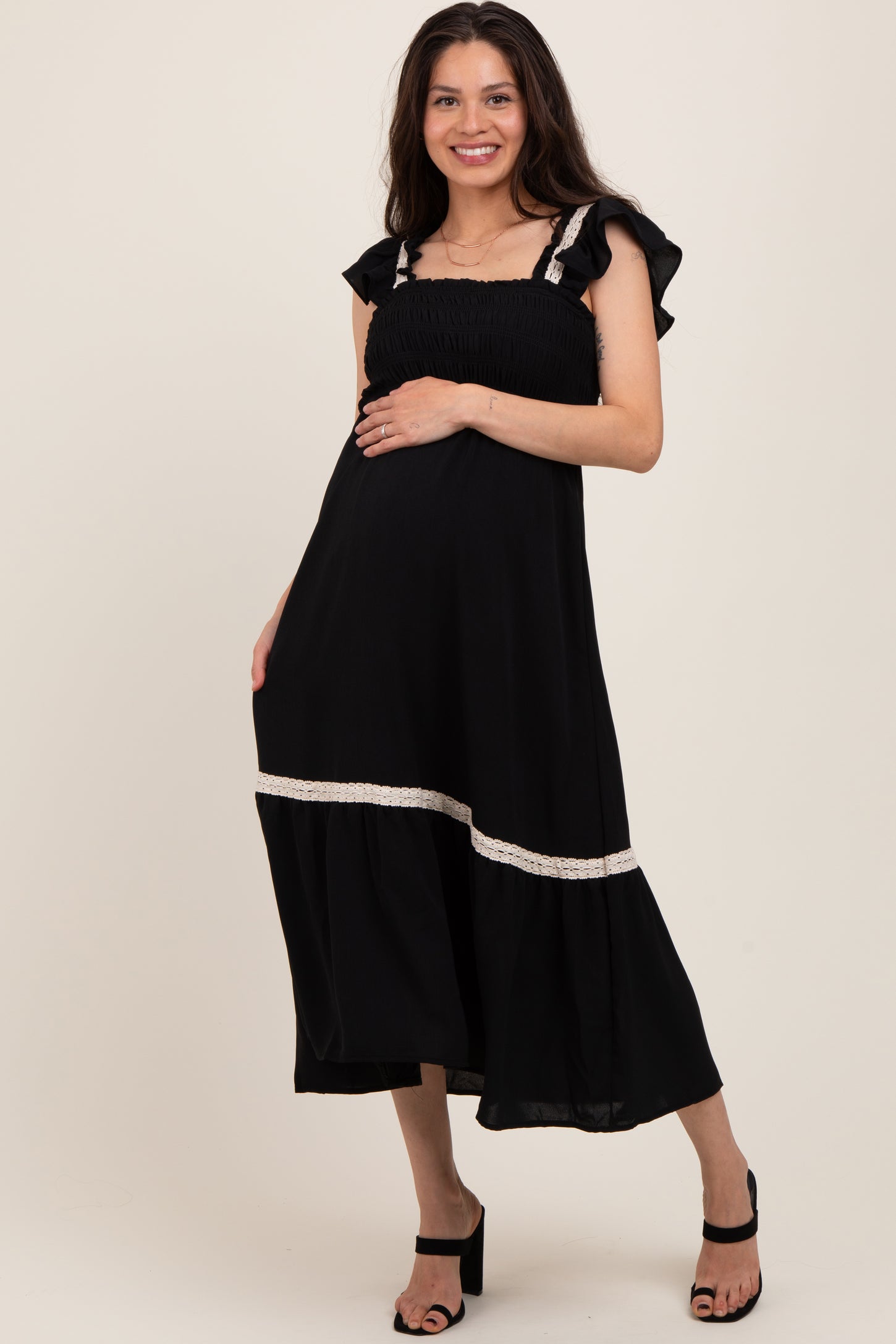 woman wearing a black maternity dress with ruffled sleeves and a tiered hem, holding her baby bump