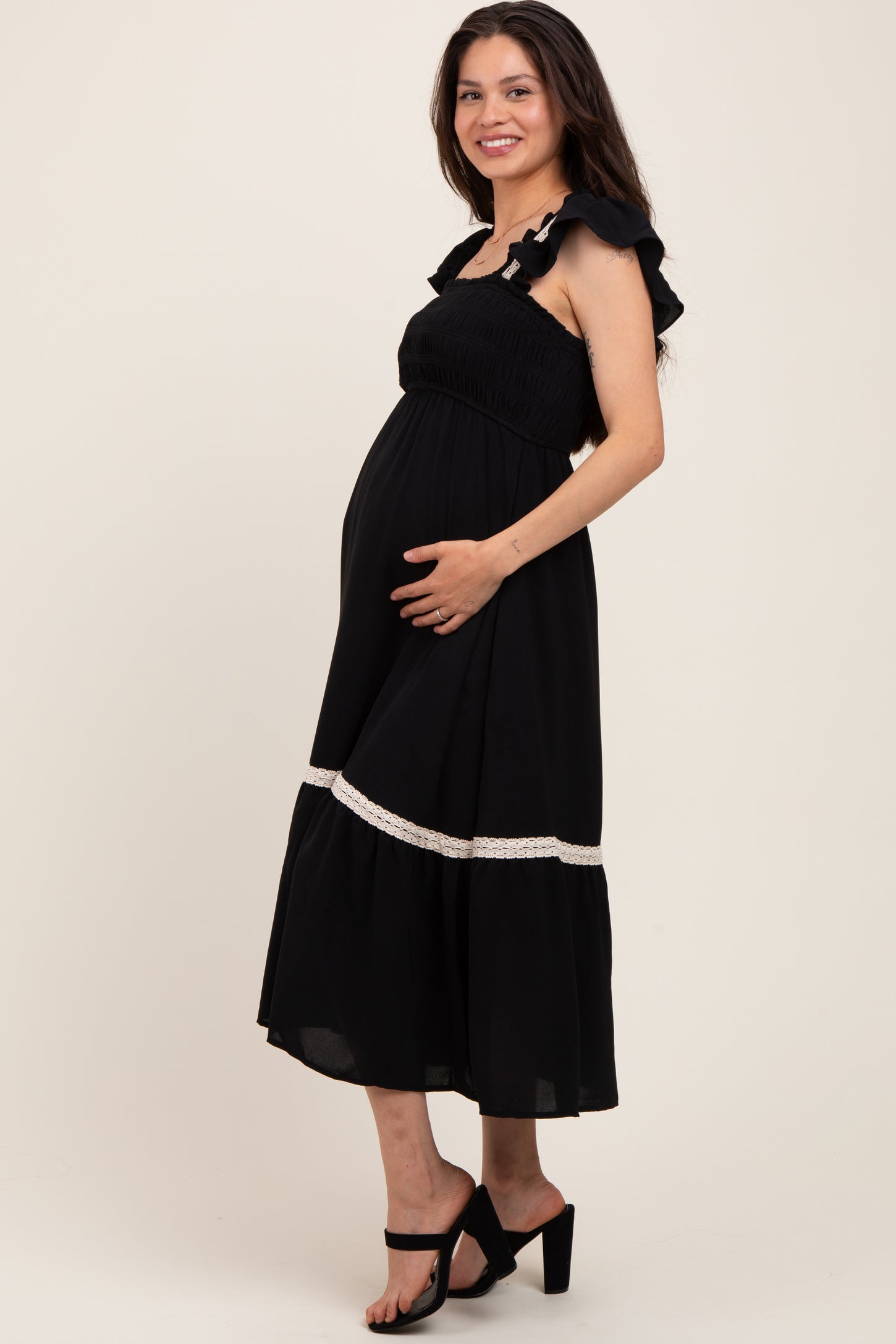 woman wearing a black maternity dress with ruffled straps and lace trim, gently holding her baby bump