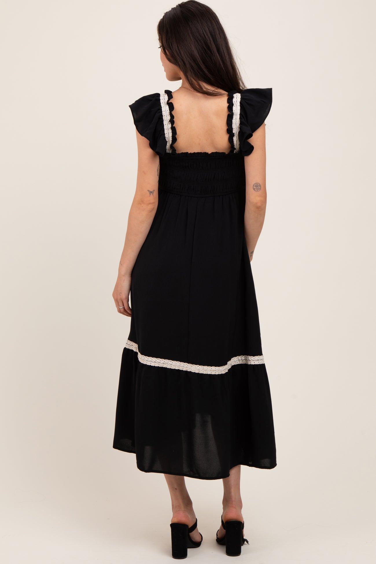woman wearing a black maternity dress with ruffled sleeves and a smocked bodice, seen from the back