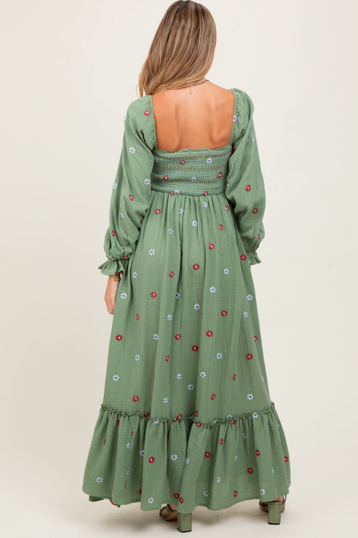 woman wearing a green maternity maxi dress with floral embroidery and smocked back detail