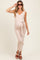 woman wearing a light pink ribbed maternity dress with a v-neck and tie waist, holding sunglasses and showing her baby bump