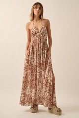woman wearing a brown floral maxi dress with a deep v-neck and side slits, standing with hands in pockets