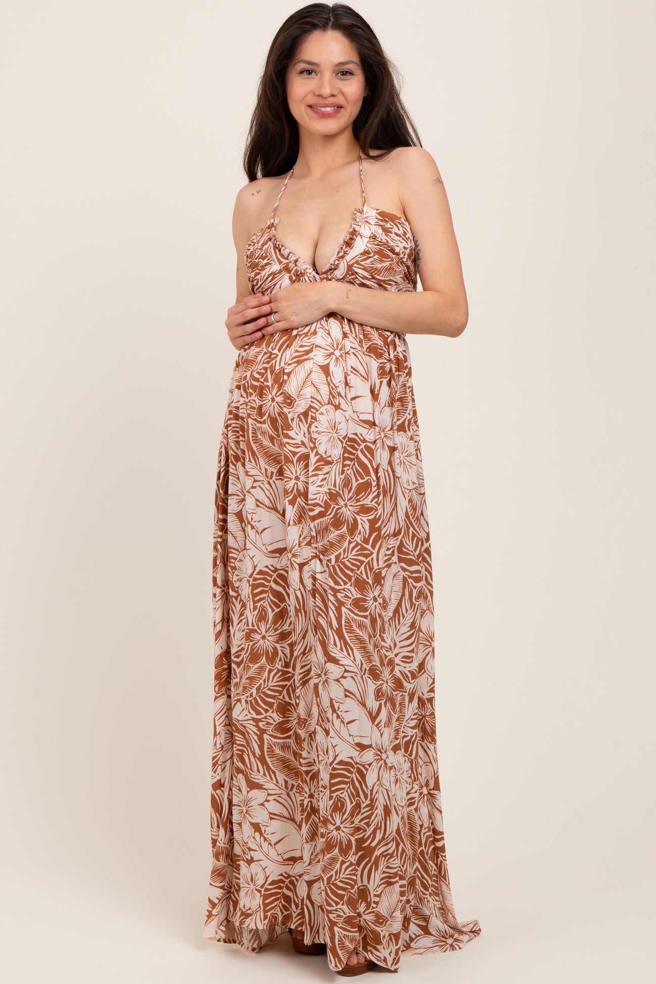 woman wearing a brown floral maternity maxi dress with a deep neckline and holding her baby bump