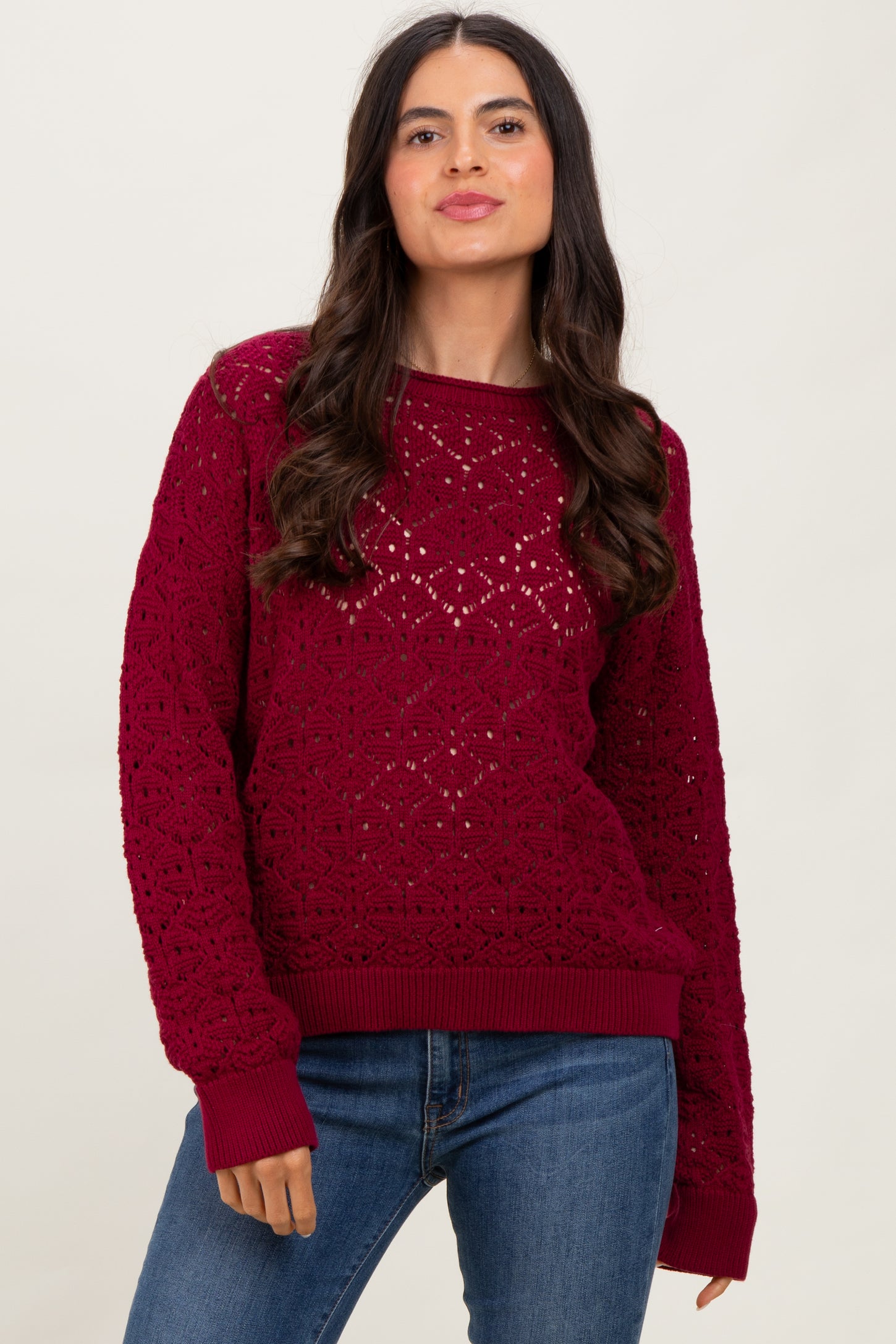 woman wearing a burgundy crochet knit sweater with ribbed cuffs and hem, paired with blue jeans