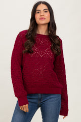 woman wearing a burgundy crochet knit sweater with ribbed cuffs and hem, paired with blue jeans