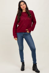 woman wearing a burgundy knit sweater with a textured pattern and blue skinny jeans, standing in black ankle boots