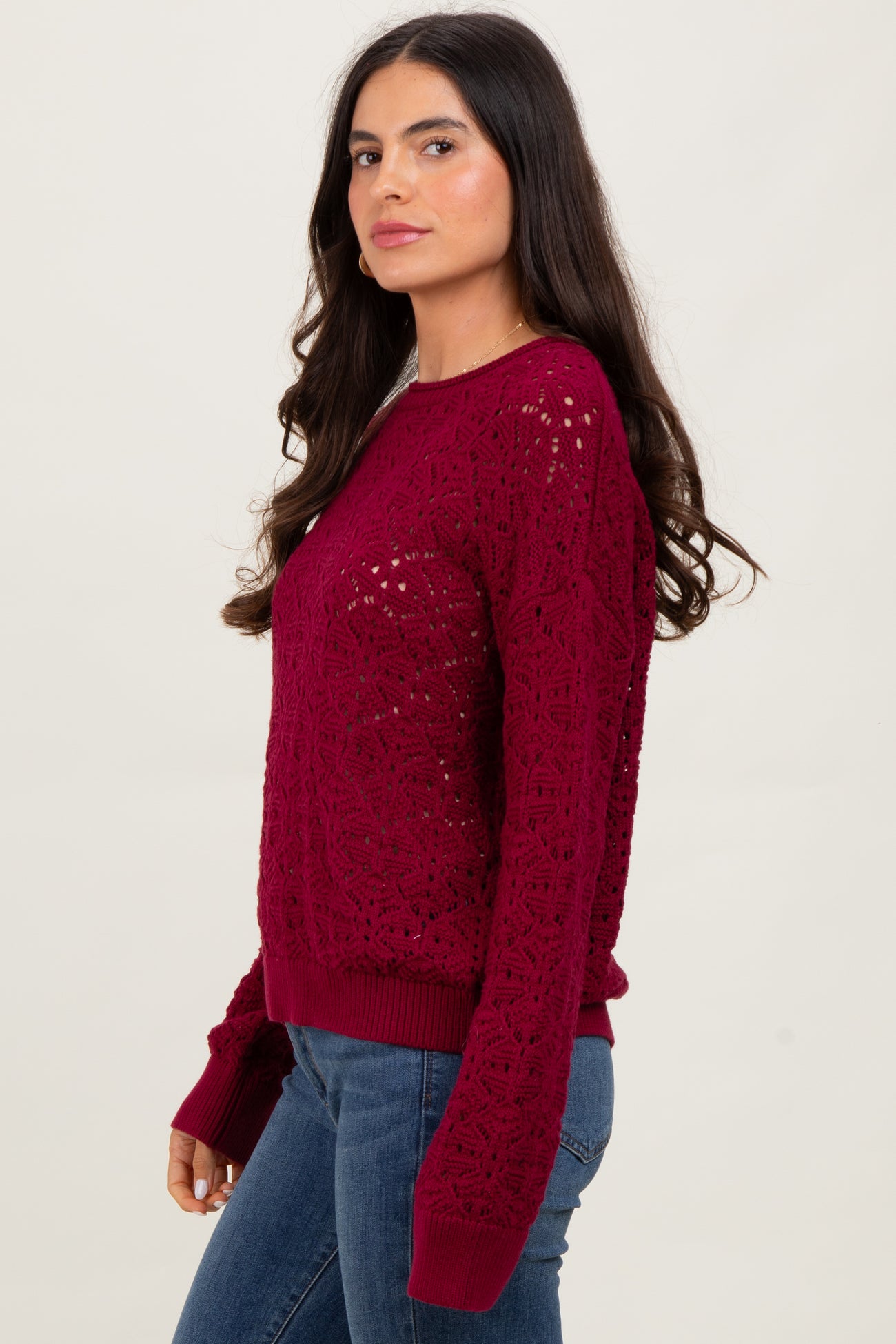 woman wearing a burgundy lace knit sweater with long sleeves and a relaxed fit, paired with blue jeans