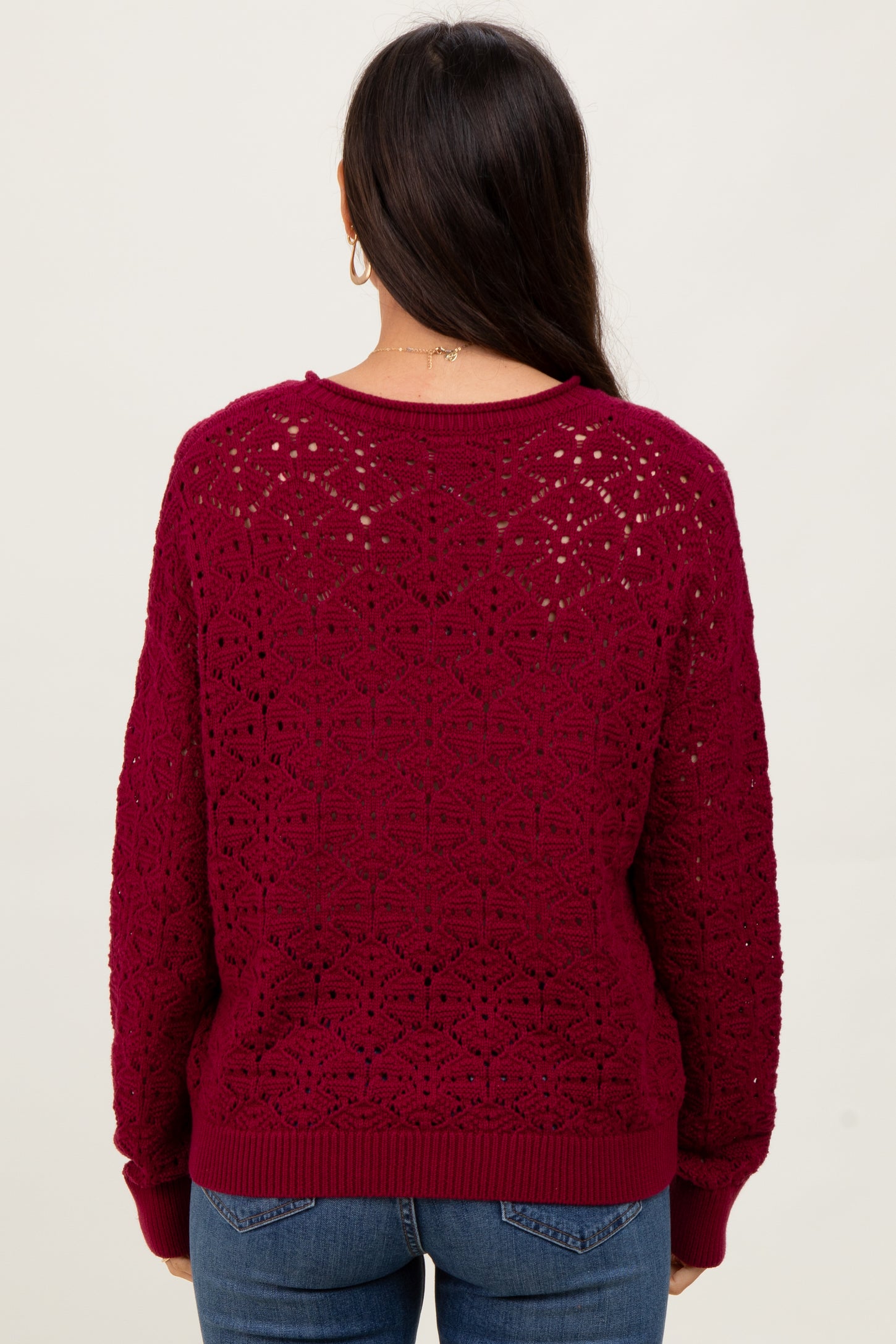 woman wearing a burgundy crochet knit sweater with a relaxed fit, viewed from the back