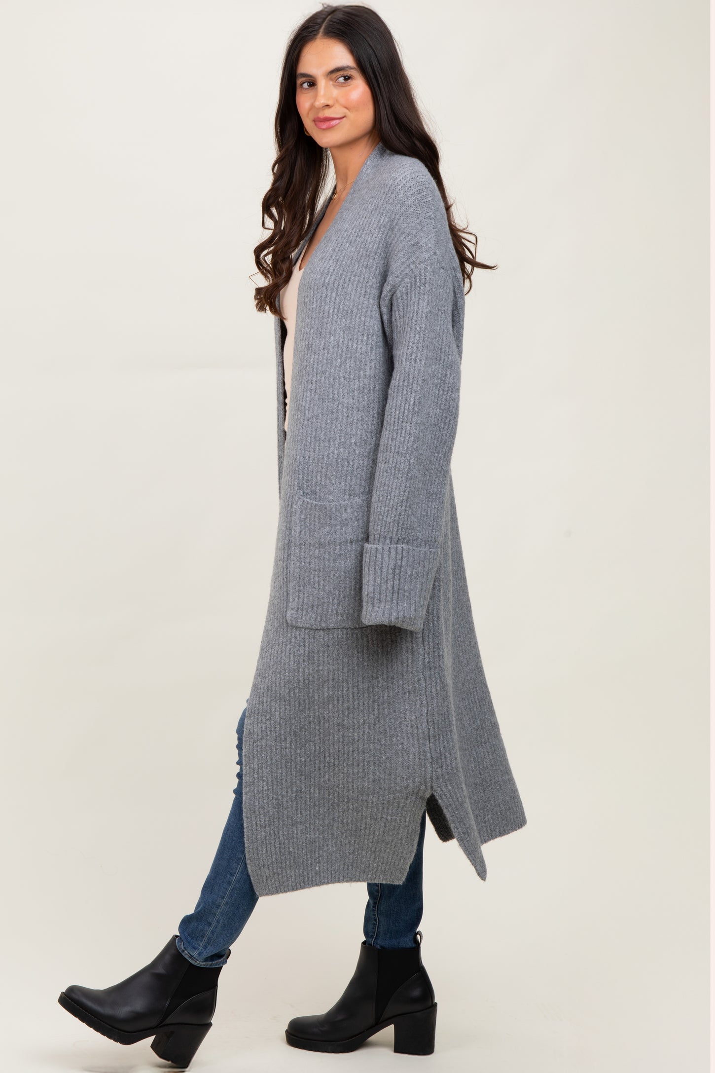 woman wearing a long gray ribbed cardigan over a beige top and blue jeans, paired with black ankle boots