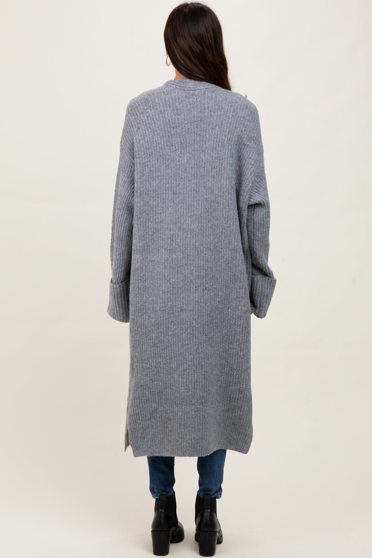 woman wearing a long gray ribbed cardigan with side slits and relaxed fit, paired with blue jeans and black ankle boots