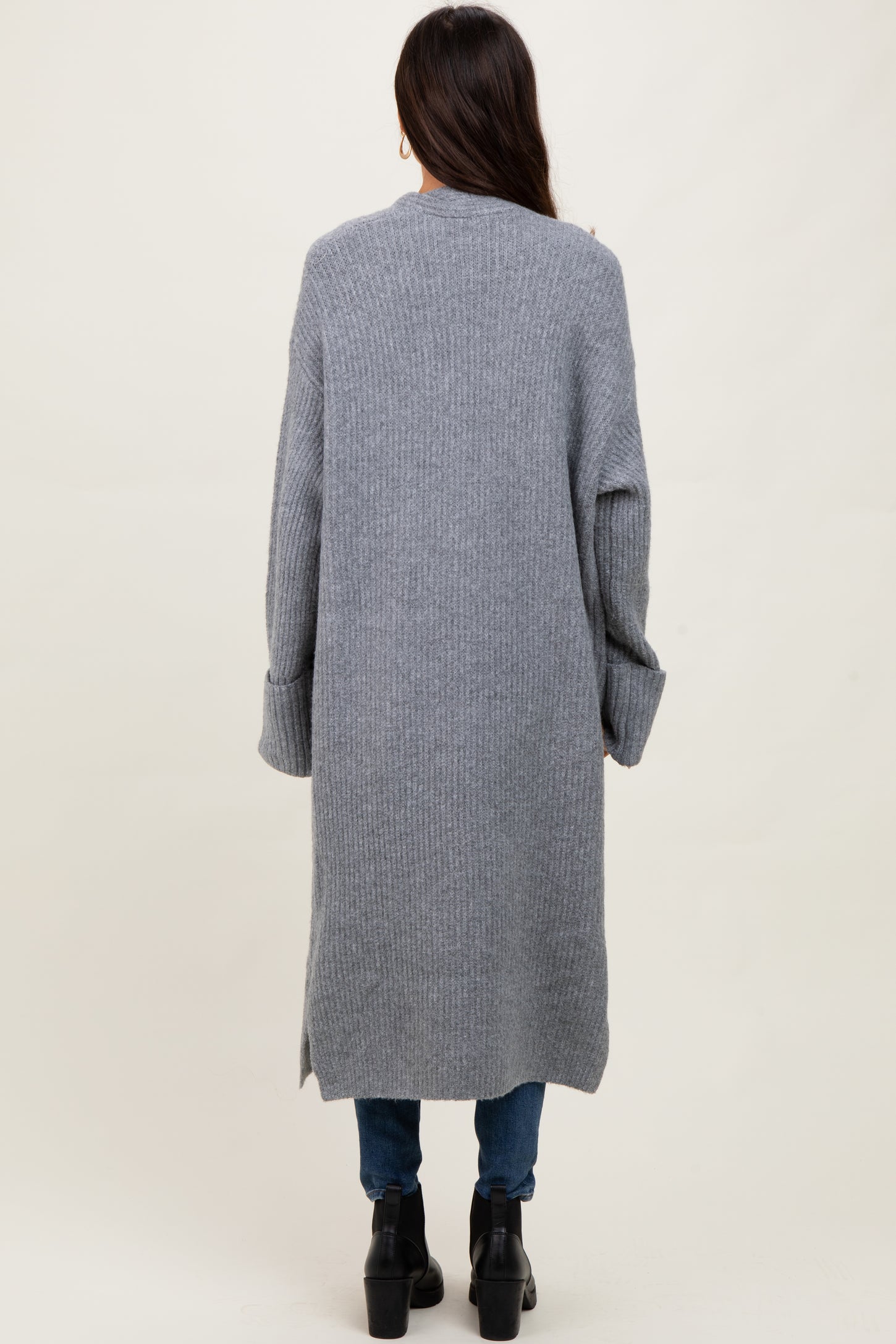 woman wearing a long gray ribbed cardigan with side slits and relaxed fit, paired with blue jeans and black ankle boots
