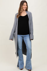 woman wearing a gray long cardigan over a black maternity top and blue flare jeans, showing her baby bump