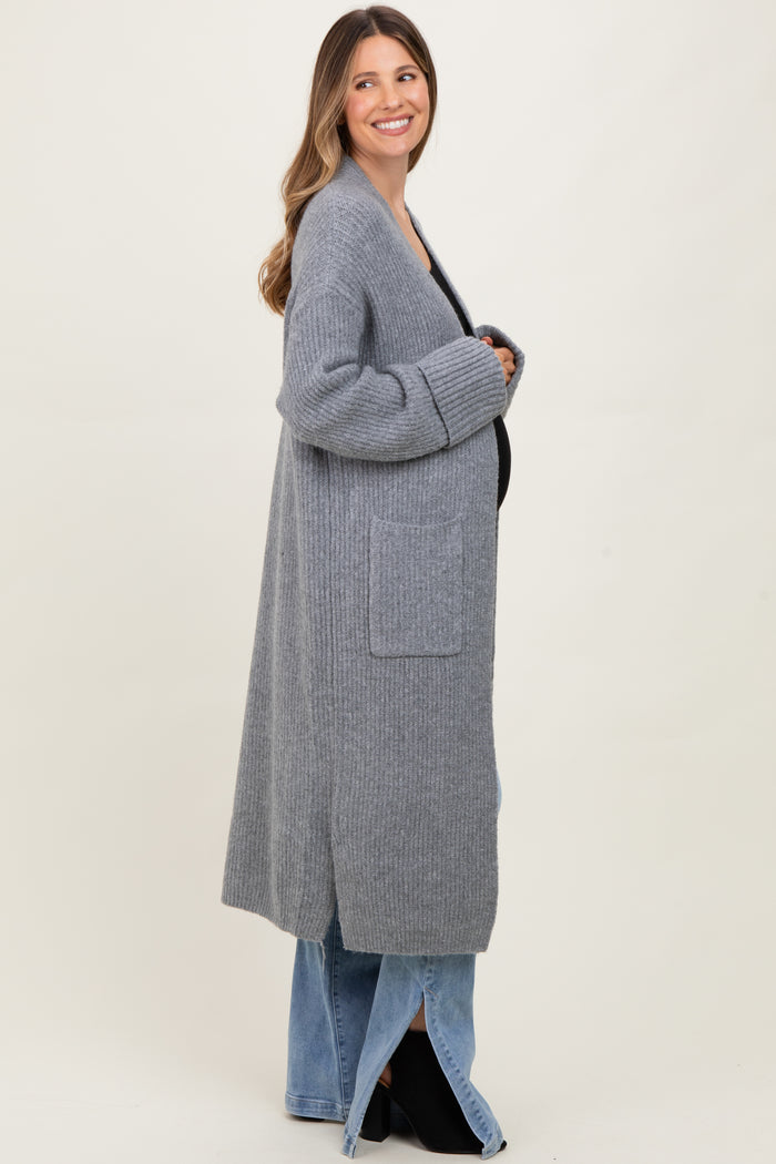 woman wearing a long gray knitted maternity cardigan over a black top, with visible baby bump and relaxed fit jeans